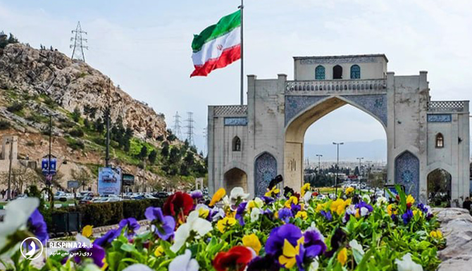 نمایی ار دروازه قرآن در روز با گل های رنگارنگ و پرچم ایران